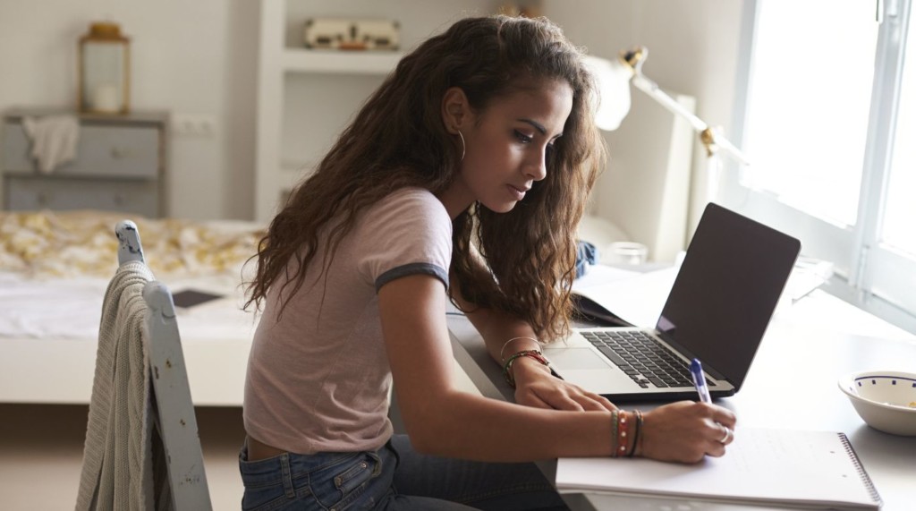 Jeune femme dans une chambre à coucher, travaillant à son bureau sur un ordinateur portable