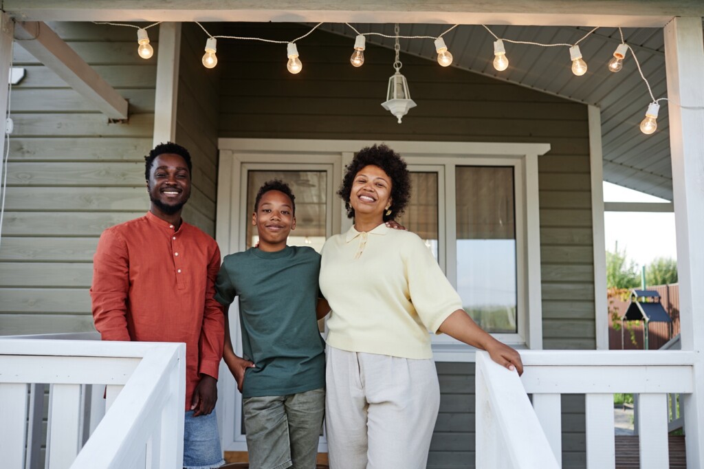 Portrait of happy black family standing on porch of new house and smiling at camera